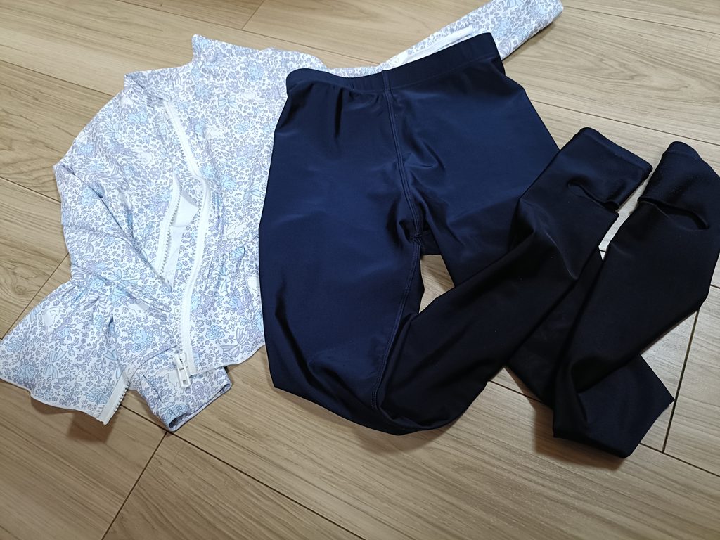 床に並べた娘の花柄ラッシュガードと紺色のラッシュトレンカ